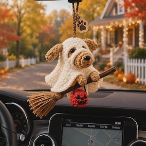 May include: A crocheted dog ornament wearing a white ghost costume, riding a brown yarn broomstick, and holding a small orange jack-o'-lantern. The ornament hangs from a brown cord with a wooden paw print charm attached to the top.
