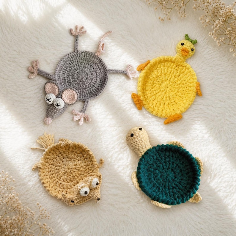 May include: Four handmade crochet coasters shaped like animals. The set includes a gray mouse with X-shaped eyes, a bright yellow duck, a tan hedgehog with a spiky back, and a green turtle with a dark green shell. Each coaster is circular.