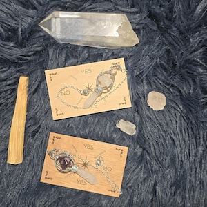 May include: An overhead shot of spiritual items on a dark blue, fluffy surface. The items include two small wooden planchette boards with "YES" and "NO" text, crystals, and a stick of palo santo incense.