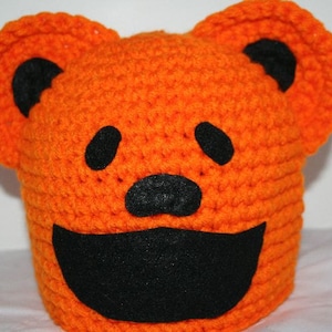 May include: Orange crocheted hat with black felt eyes, nose, and mouth, shaped like a smiling pumpkin.