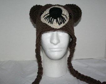 May include: Brown crocheted hat with a bear face and long brown tassels. The bear face has a black nose and white whiskers.