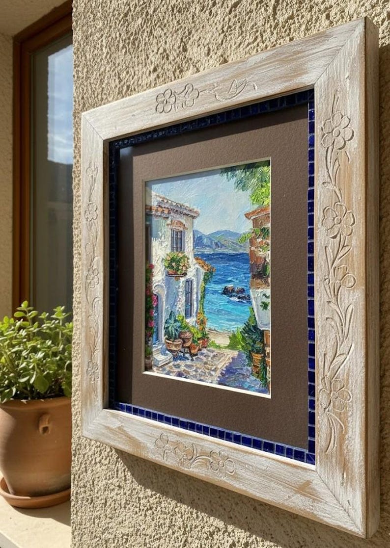 May include: A square wall art piece featuring a textured painting of a Mediterranean coastal scene with white buildings and blue sea. The artwork is encased in a light-colored, distressed wooden frame with carved floral details and a blue mosaic border.