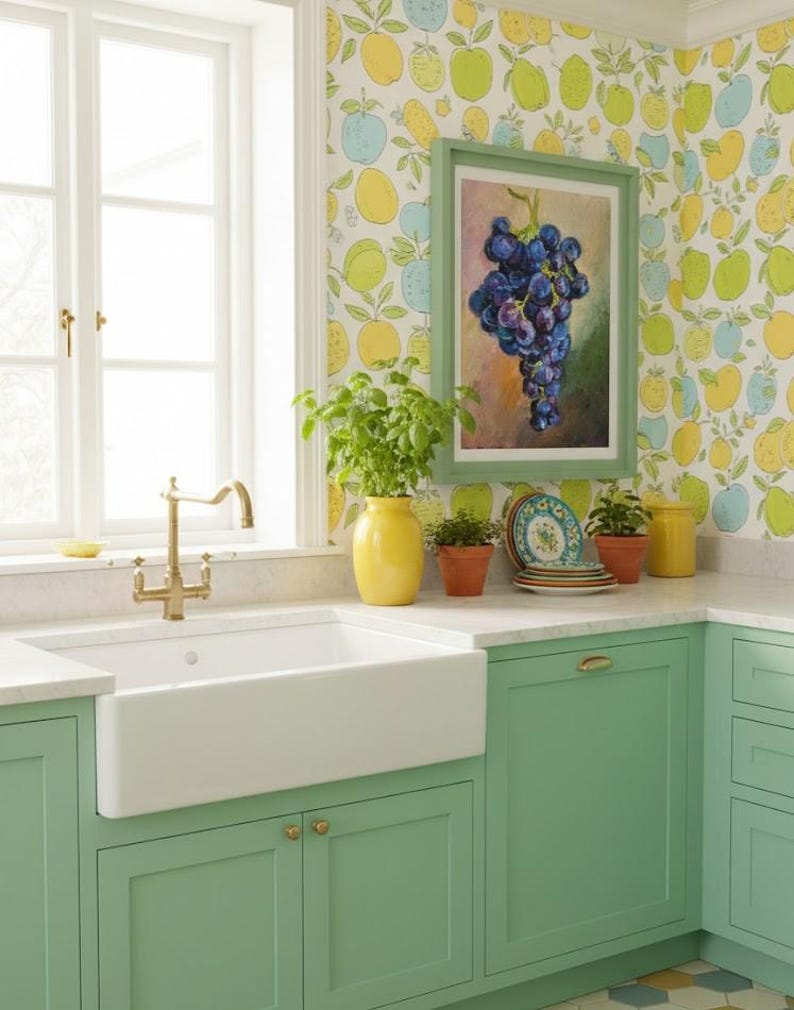 May include: A kitchen featuring mint green cabinets, a white farmhouse sink with a brass faucet, and a yellow vase with a green plant. The wall has fruit-patterned wallpaper and a framed oil painting of a bunch of dark purple grapes.