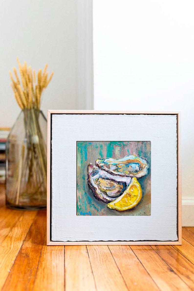 May include: Oil painting of oysters and a lemon slice. The artwork features a square canvas with a white border and a light brown frame. The painting has a teal and brown background with the oysters and lemon in the foreground.