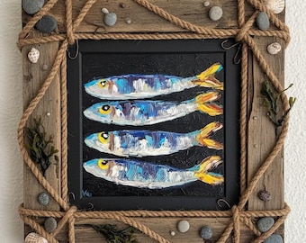 May include: A square painting of four blue and yellow fish on a black background, set in a rustic wooden frame wrapped in thick jute rope. The frame is decorated with small grey pebbles, white seashells, and dried seaweed pieces.