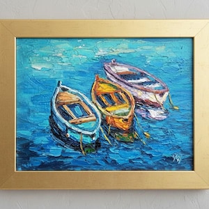 May include: An oil painting in a gold frame depicting three small rowboats floating on textured blue water. The boats are colored light blue, yellow, and white with visible brushstrokes. The scene captures a calm maritime view.