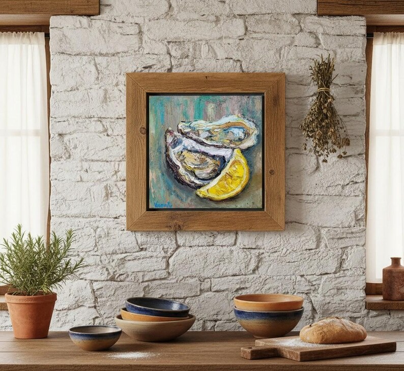 May include: A framed painting of oysters and a lemon slice. The artwork is in a wooden frame and hangs on a white brick wall. A small potted plant, bowls, and a loaf of bread are on a wooden surface.