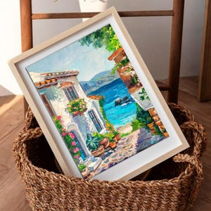 May include: An oil painting in a light wood frame depicting a coastal scene with a white building, vibrant pink and green flowers, a stone path, and a bright blue sea under a clear sky, rendered with thick, visible brushstrokes and texture.
