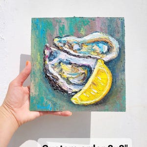 May include: An 8x8 inch oil painting of oysters and a lemon slice. The artwork features textured brushstrokes with a palette of blues, yellows, and whites. The painting is held by a hand against a white background. Text on the painting reads "Custom order 8x8".