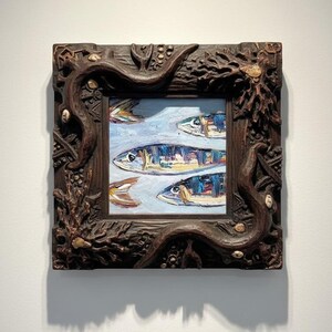 May include: An oil painting of several fish swimming in a light blue background. The fish are painted with blue, yellow, and white brushstrokes. The painting is framed in a dark brown, ornate wooden frame with carved details.