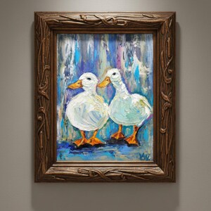 May include: Oil painting of two white ducks with orange beaks and feet, set against a blue and purple background. The artwork is framed in a dark brown, ornate wooden frame, adding a classic touch to the piece.
