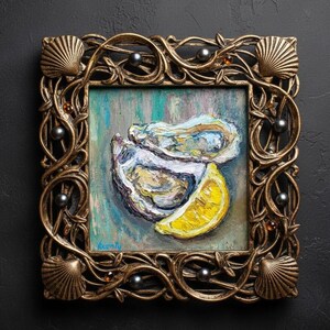 May include: Square framed oil painting of oysters and a lemon wedge. The painting is in a gold ornate frame with seashell and pearl accents. The painting has a teal, blue, and yellow color palette.