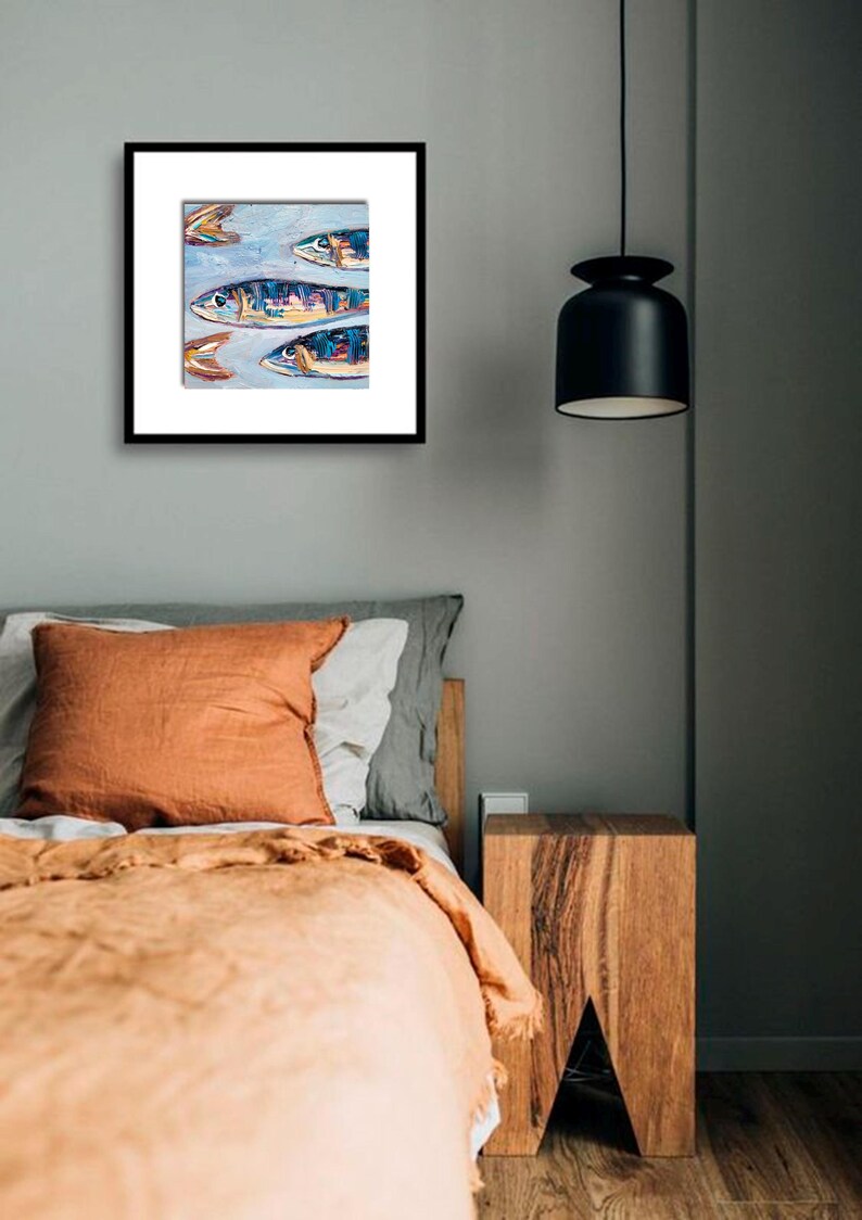 May include: A framed artwork featuring an abstract painting of several fish in shades of blue, yellow, and orange. The artwork is displayed on a gray wall above a bed with orange and gray bedding. A black pendant light hangs from the ceiling.