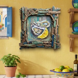 May include: A framed artwork depicts an oyster and lemon slice. The frame is made of driftwood pieces. The artwork is mounted on a yellow wall. A small potted plant and a bowl of lemons are in the foreground.