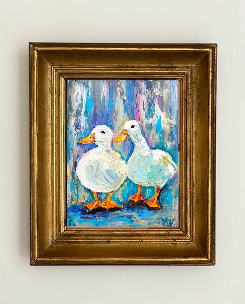 May include: Oil painting of two white ducks with orange beaks and feet, set against a colorful background of blues, purples, and turquoise. The artwork is framed in a gold-colored, ornate frame, adding a touch of elegance to the piece. The painting is signed in the bottom right corner.