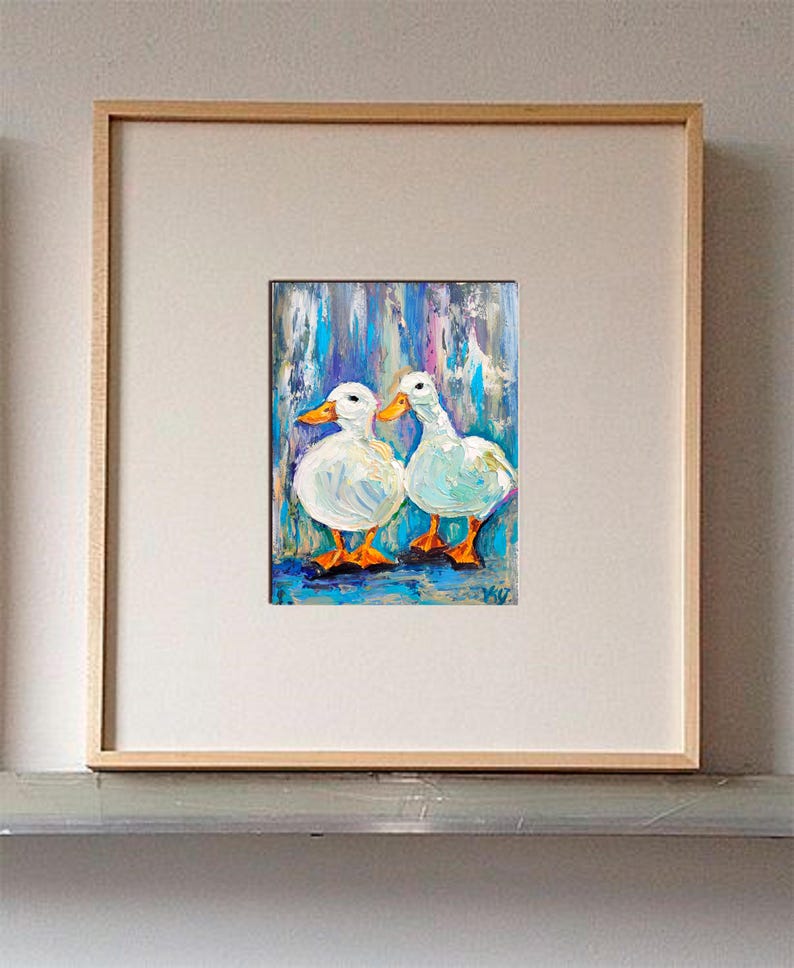 May include: An oil painting of two white ducks with orange beaks and feet, set against a blue and purple background. The artwork is framed in a light wood frame and matted with a white border.