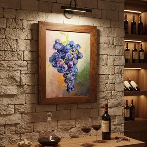 May include: A framed oil painting of a cluster of purple grapes hanging on a vine, displayed on a stone wall. The artwork features textured brushstrokes in shades of blue, violet, and green, enclosed in a simple, medium-toned wooden frame.