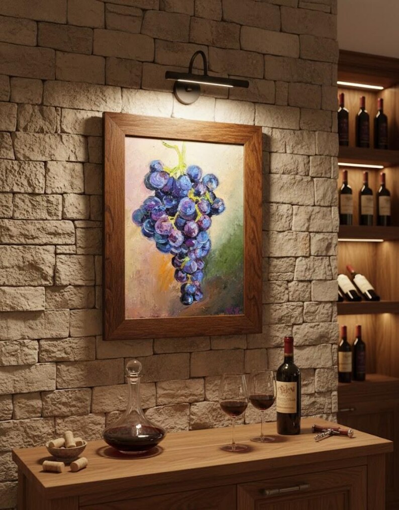 May include: A framed oil painting of a cluster of purple grapes hanging on a vine, displayed on a stone wall. The artwork features textured brushstrokes in shades of blue, violet, and green, enclosed in a simple, medium-toned wooden frame.