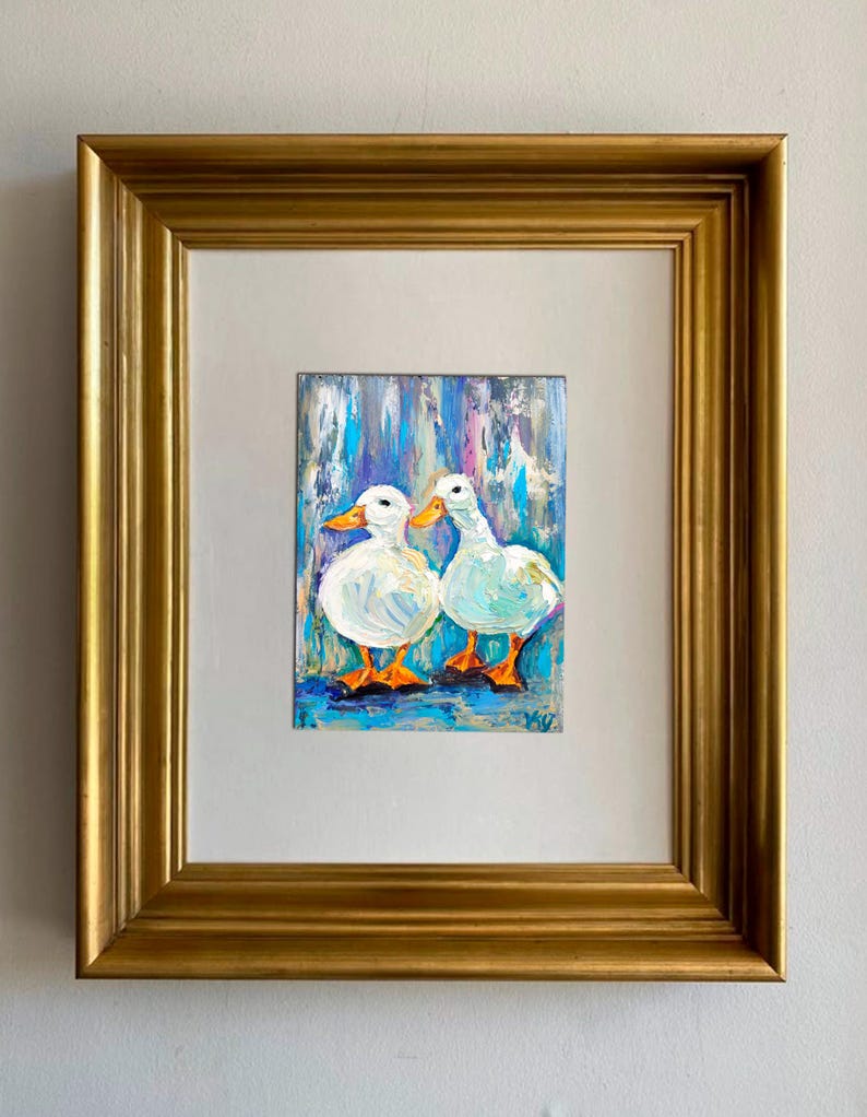 Oil painting of two white ducks with orange feet and beaks, set against a blue and white background. The artwork is framed in a gold-colored, ornate frame, creating a decorative piece.