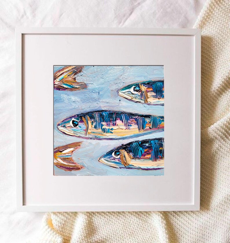 May include: An original oil painting of several fish swimming in a light blue sea. The fish are painted with textured brushstrokes in shades of blue, yellow, and orange. The artwork is framed in a white square frame.