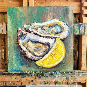 May include: Square 8x8 inch oil painting of oysters and a lemon slice. The artwork features thick brushstrokes in shades of white, yellow, and green. The painting is on a wooden easel. Text on the painting reads "Custom order 8x8".