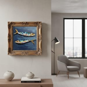 May include: An oil painting in a decorative gold frame featuring two fish with blue, yellow, and white scales against a dark blue background. The artwork displays visible brushstrokes and thick paint texture, capturing the fish in a horizontal orientation.