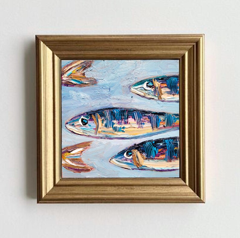 May include: Square framed oil painting of several fish swimming in a light blue sea. The fish are painted with blue, orange, and yellow brushstrokes. The frame is gold.