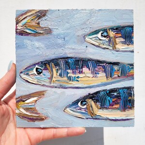 A painting of three fish on a blue background. The fish are painted in a realistic style with details of their scales and fins. The fish are arranged in a vertical line, with the largest fish at the top and the smallest fish at the bottom.
