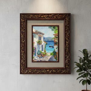 May include: A framed oil painting depicting a coastal Mediterranean scene with white buildings, potted plants, and a blue sea. The artwork is encased in a dark brown, ornate, carved wooden frame with a textured beige matting surrounding the image.