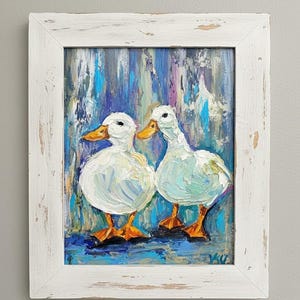May include: Oil painting of two white ducks with orange beaks and feet, set against a blue, purple, and teal background. The artwork is framed in a distressed white wooden frame, adding a rustic touch to the piece.