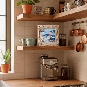 May include: A kitchen scene featuring wooden shelves with mugs, a framed fish painting, and copper pots. A silver espresso machine sits on the counter, with a glass jar of coffee beans. Plants in terracotta pots add a touch of greenery.