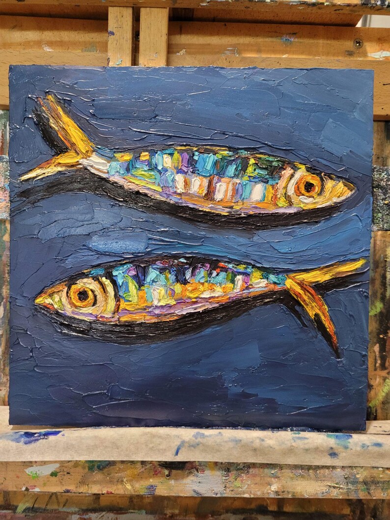 May include: An oil painting on canvas featuring two fish swimming in opposite directions against a dark blue background. The fish are rendered with thick, textured impasto brushstrokes in vibrant shades of yellow, orange, blue, and purple.