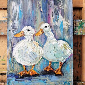 Oil painting of two white ducks with orange beaks and feet. The ducks are painted with thick brushstrokes, giving them a textured appearance. The background is a blend of blue, purple, and white vertical strokes.