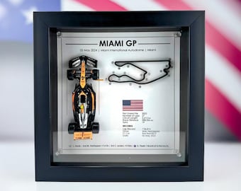 May include: A framed display featuring a miniature Formula 1 race car in orange and black with the text "MIAMI GP" and a track map. The text below the map includes details about the race, including the date, circuit length, and lap record.