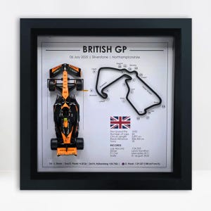 Puede incluir: Obra de arte enmarcada que muestra un coche de carreras de Fórmula 1 negro y naranja, un mapa de la pista y detalles del Gran Premio de Gran Bretaña. El texto incluye la fecha, la ubicación y las estadísticas de la carrera.