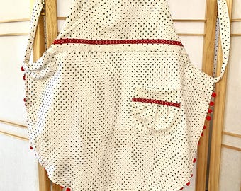 May include: A white apron with black polka dots and red trim. The apron has a red pom-pom trim around the bottom and a red pocket with a white ruffle.