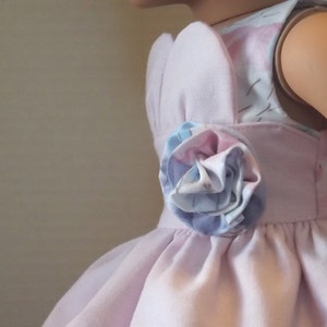 以下が含まれることがあります： 側面に花柄のディテールが付いたピンクのドレス。ドレスはノースリーブのボディスとフルスカートです。