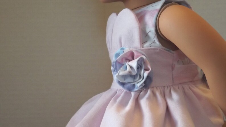 以下が含まれることがあります： 側面に花柄のディテールが付いたピンクのドレス。ドレスはノースリーブのボディスとフルスカートです。