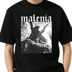 Puede incluir: Camiseta negra con un diseño en escala de grises de un guerrero con un casco con cuernos y el texto "malenia goddess of rot" en blanco. El diseño está centrado en la parte delantera de la camiseta.