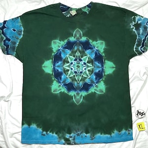 May include: Green tie-dye t-shirt with a large, symmetrical mandala design in shades of blue and green. The sleeves and bottom hem feature blue tie-dye accents. The shirt is labeled XL.