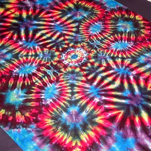 May include: A colorful tie-dye fabric with a repeating pattern of concentric circles and radiating lines in shades of red, yellow, blue, and black.