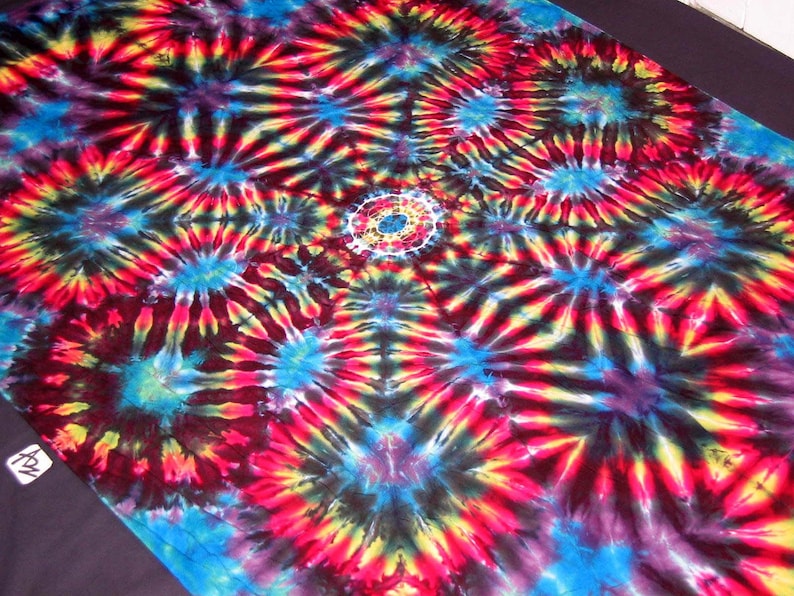 May include: A colorful tie-dye fabric with a repeating pattern of concentric circles and radiating lines in shades of red, yellow, blue, and black.
