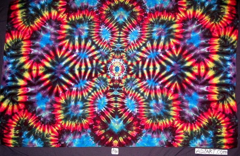 May include: A colorful tie-dye fabric with a symmetrical pattern of red, yellow, blue, and black swirls. The fabric has a central design with a smaller circle in the middle.