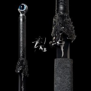 Może przedstawiać: Czarny miecz katana z rękojeścią w kształcie głowy smoka i niebieskim okiem na jelec. Miecz jest owinięty w czarną tkaninę z ozdobnym wzorem.