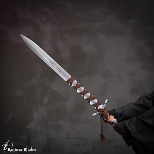 May include: A silver sword with a brown leather wrap on the handle. The sword is held by a person wearing a black jacket.