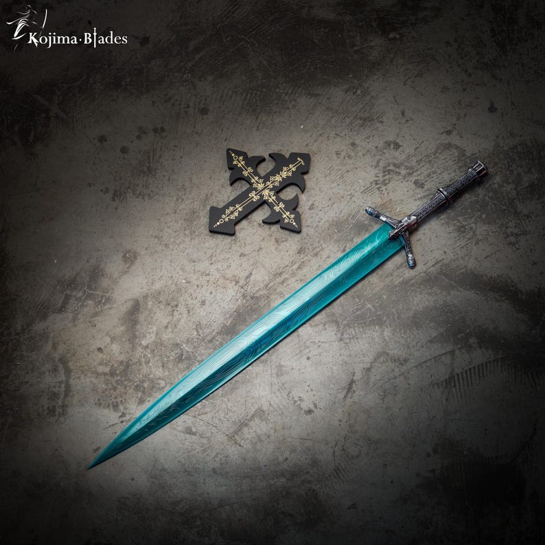 May include: A teal-colored sword with a black handle and a silver cross guard. The sword is lying on a gray surface with a black cross with gold accents in the background. The text "Kojima Blades" is visible in the top left corner of the image.