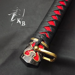 May include: Close-up of a black and red sword handle with a gold accent. The handle is wrapped in black leather with red stitching and has a decorative gold piece at the end.