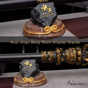 May include: Resin display stands for a staff, featuring a black rock with gold text that reads "Black Myth Wukong." The stands have a brown base with gold accents and a decorative gold band. The text "Ruyi Jingu Bang Resin Display Stands" is also visible.