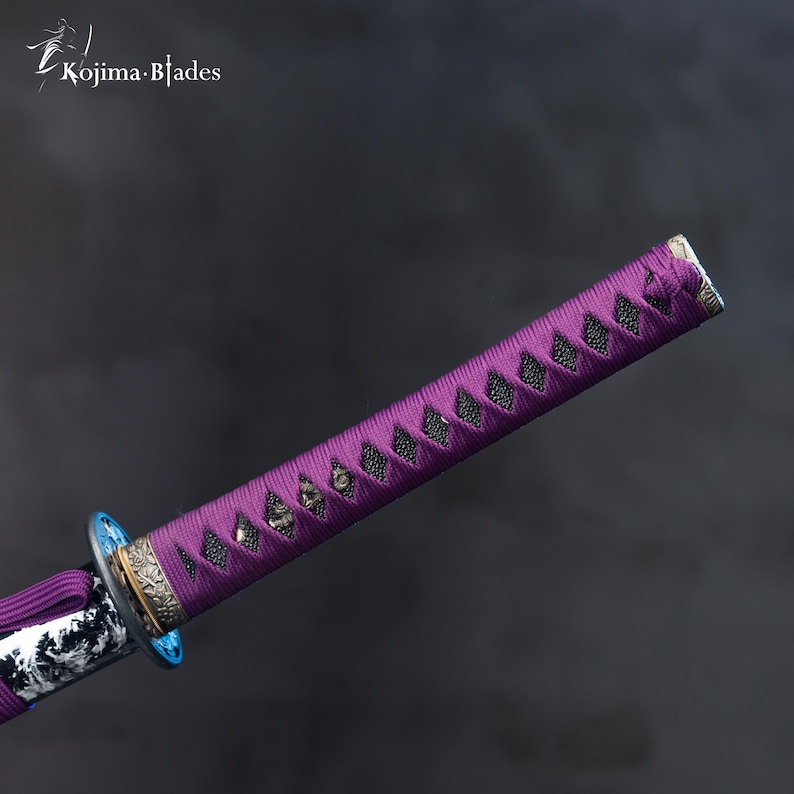 Pu&ograve; includere: Primo piano di un'impugnatura di katana viola con un rivestimento a motivi bianco e nero. L'impugnatura &egrave; decorata con un pezzo di metallo argentato e un accento blu.
