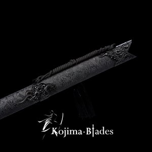 May include: Black katana sword scabbard with a dragon design and black cord. The scabbard is made of metal and has a textured surface. The cord is tied around the scabbard and has a tassel at the end. The scabbard is on a black background. "Kojima Blades" is printed in white on the bottom of the image.